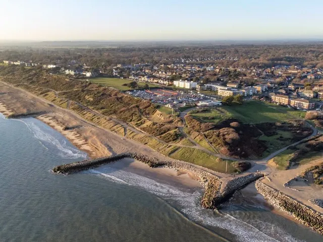 Looking west along Highcliffe Beach from the clifftop, with the sloped access paths running through gorse towards the shingle